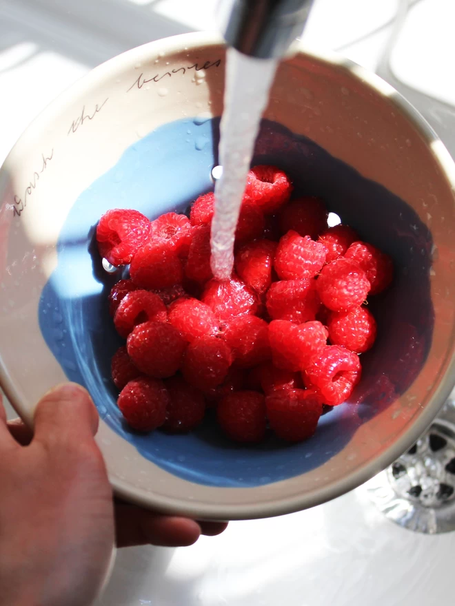 ceramic berry bowl in use in kitchen sink washing raspberries