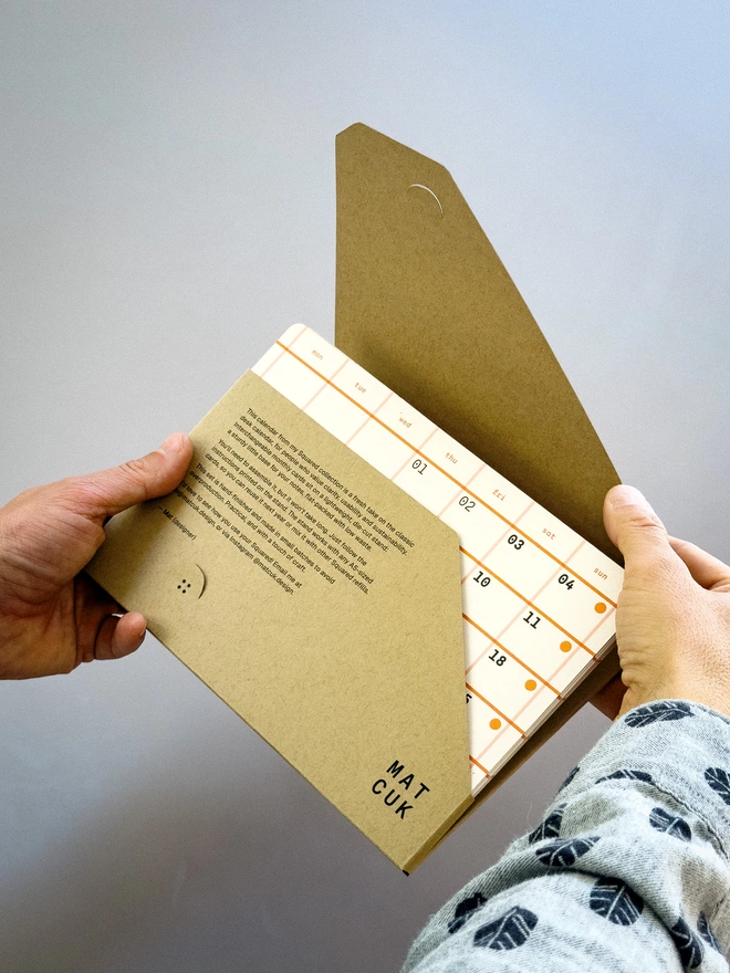Squared: hands unwrapping the calendar, orange cards visible in the packaging