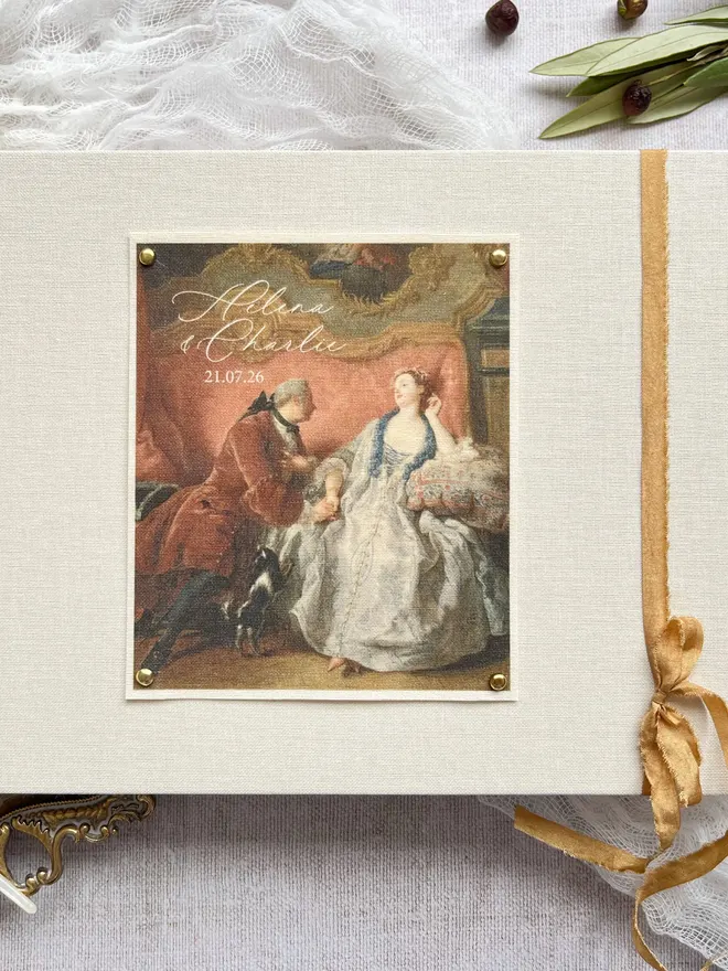 Linen wedding guest book with romantic rococo scene and gold ribbon