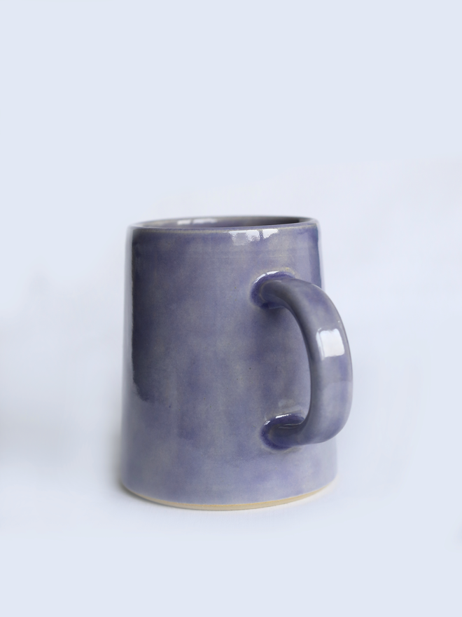 A handmade ceramic pint mug in amethyst purple glaze with a chunky loop handle, photographed against a plain light grey background