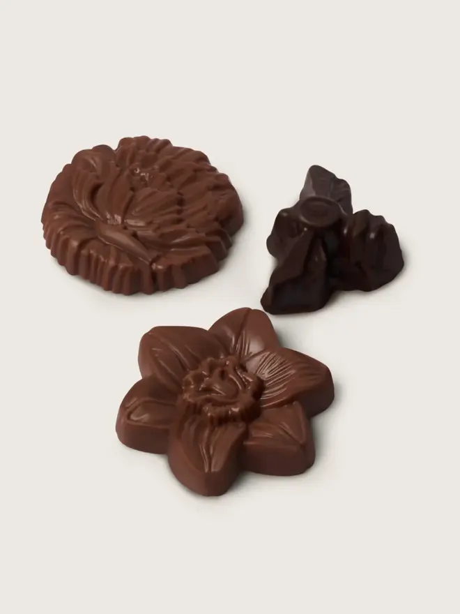 3 single handcrafted chocolates in a group shot - 2 milk chocolate flowers accompanied by a dark chocolate bee
