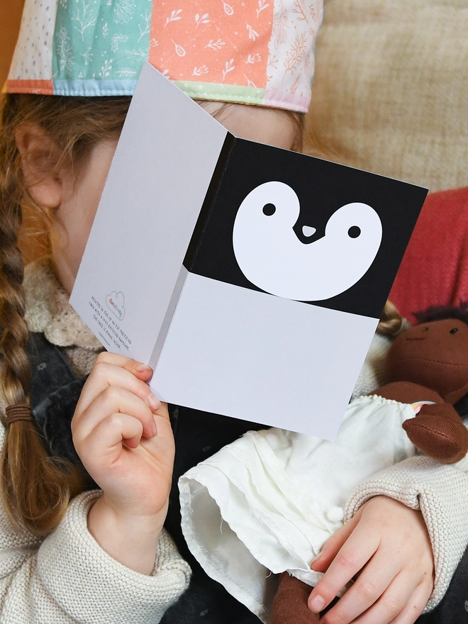 A child wearing a patchwork crown holds a penguin greetings card in front of them.