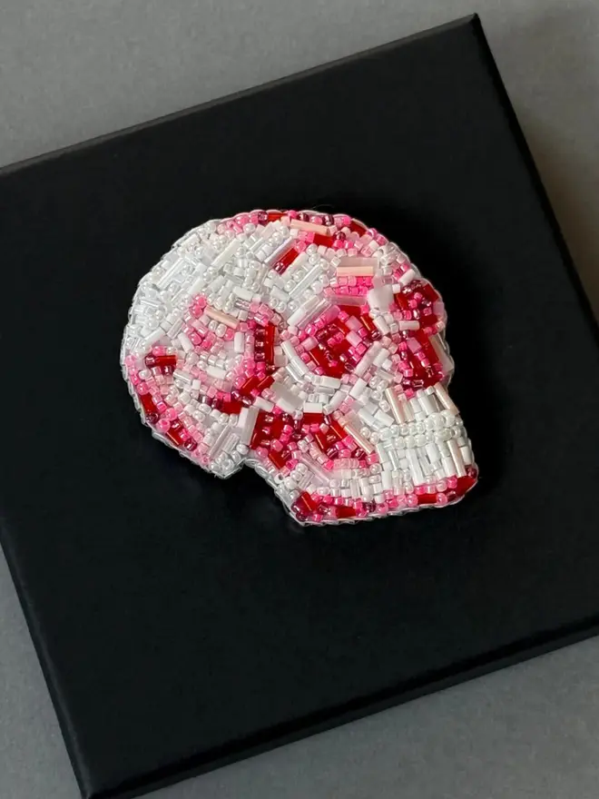 Beaded Pink Skull Brooch, displayed on a black box, against a plain background. 