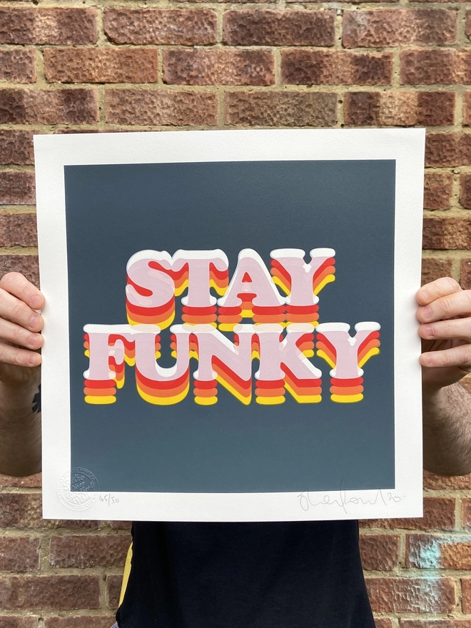 "Stay Funky" Hand Pulled Screen Print square with grey background and the words stay funky printed on top in retro letters in shadings of orange yellow and red 