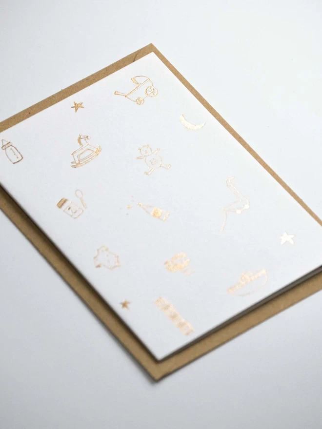 A6 Gold foil new baby card. Linear doodle of baby associated icons. Close up.