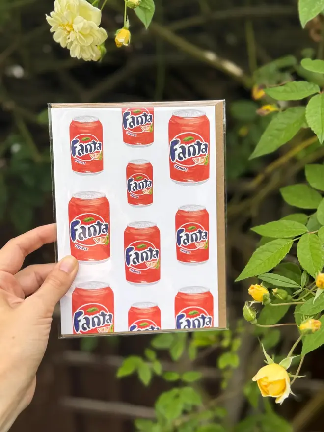 fanta cans illustrated card. card photographed against rosebush backdrop.