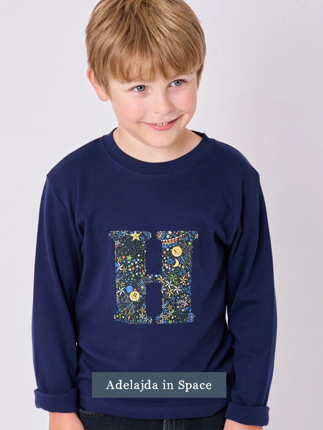 a 7 year old boy wearing a personalised kids personalised navy t-shirt with an initial cut from space liberty print on the front