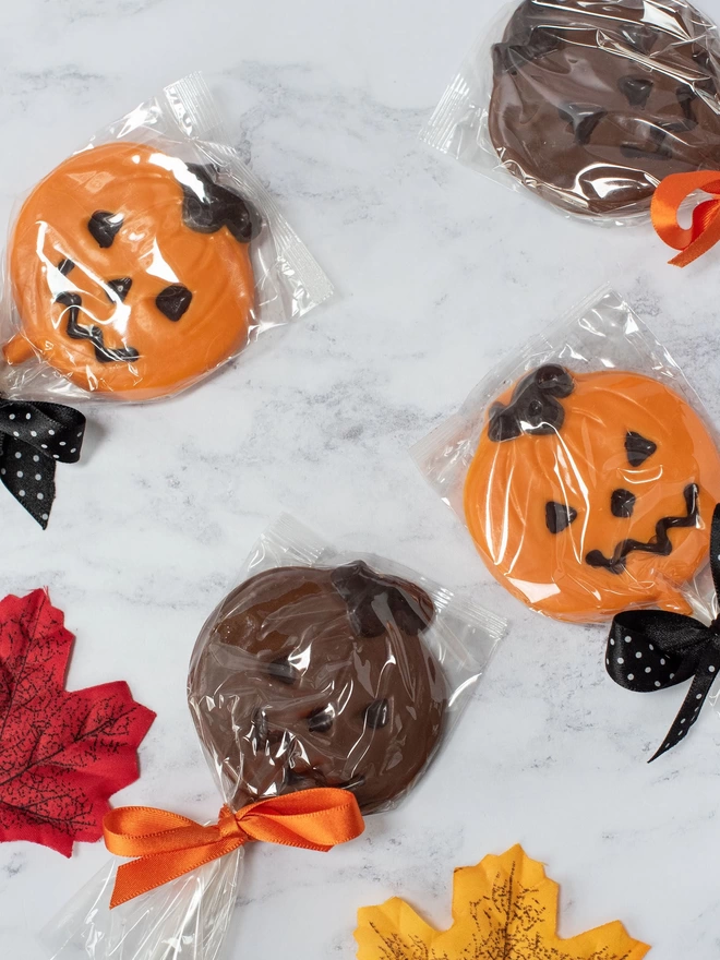 Orange and milk chocolate pumpkin lollipops surrounded by leaves