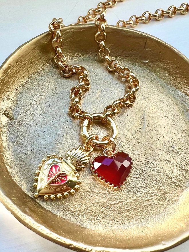 Chunky gold charm necklace on small gold bowl with two red heart charms