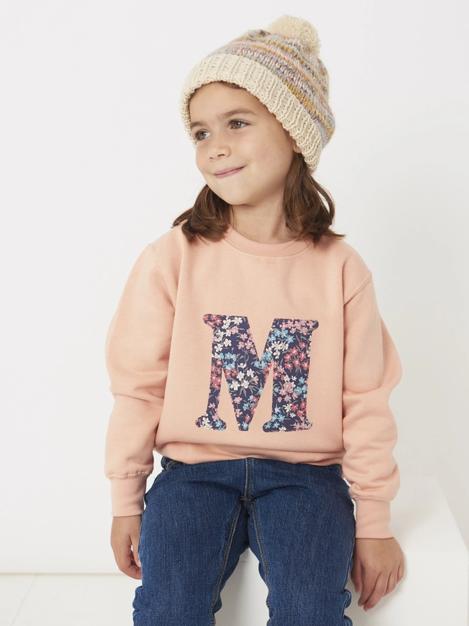a 4 year old girl wearing a personalised dusty pink sweatshirt with her initial sewn on the front in floral liberty print 