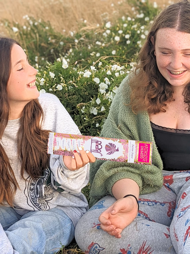 2 girls in field holding passion power well being charity incense sticks inc pink & gold illustrations