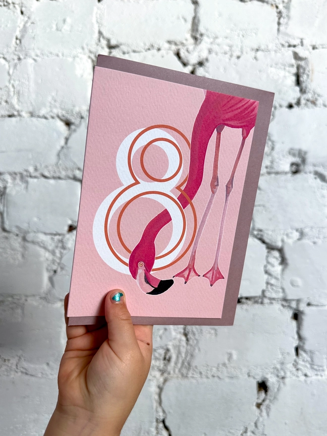 a pink card with a big white number 8 and an illustrated flamingo with a purple envelope