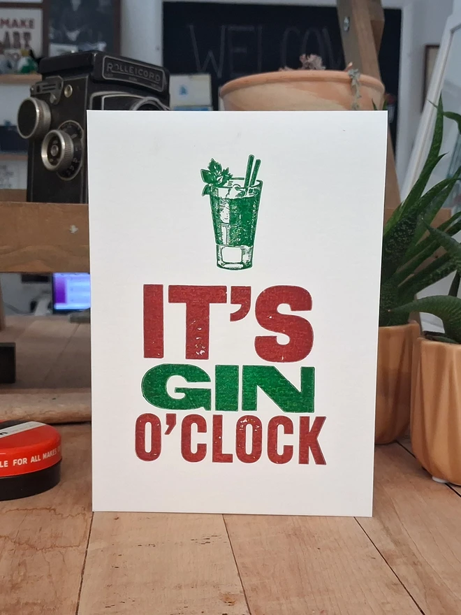 A greetings card printed in burgundy and green with the text 'It's Gin O'Clock'