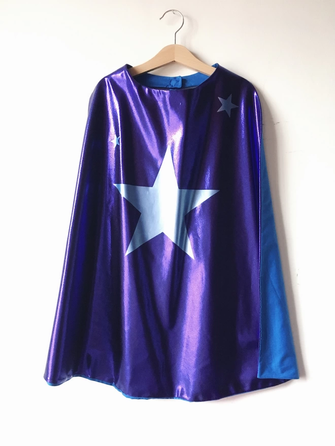 hanging purple Superhero cape with blue lining and silver star design on the back