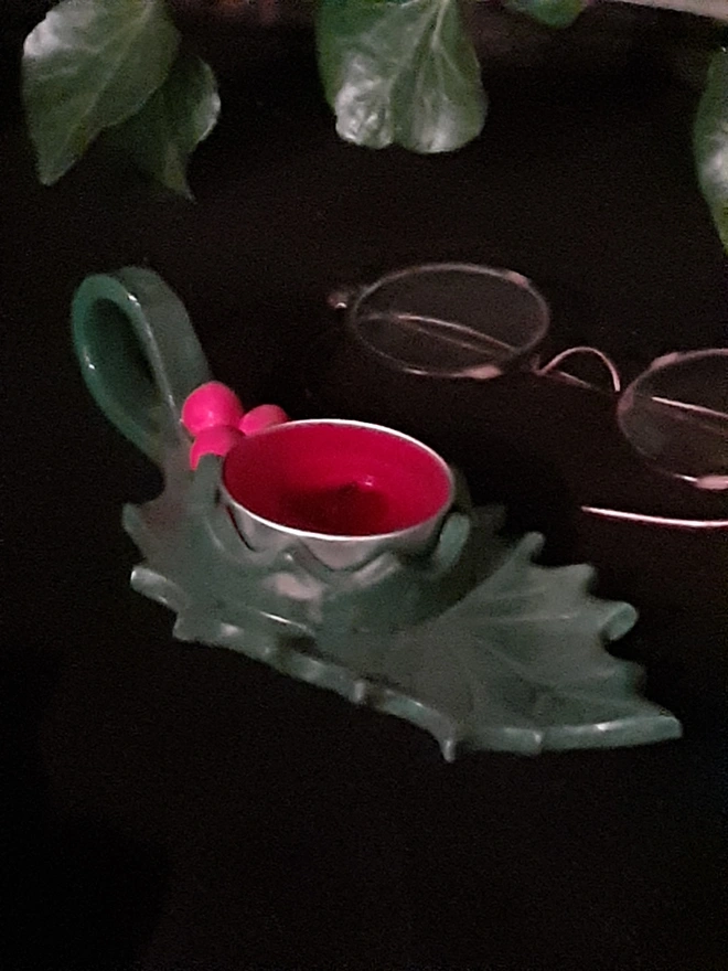 Close-up of a green glazed ceramic holly candle holder showing sculpted leaf veins, red berries and a red tealight.