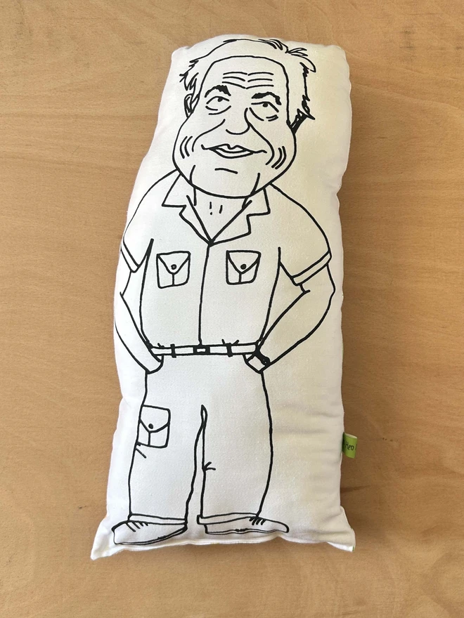 Black and white illustrated screen printed cushion of Sir David Attenborough. The cushion sits on a light wood surface.