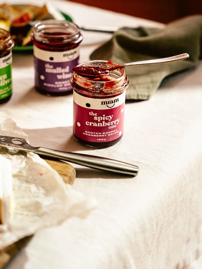 Spicy cranberry sauce in a jar with a spoon on a wooden board with cream-coloured cloth