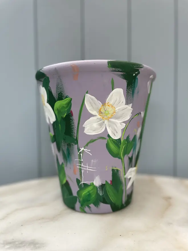 Unique hand-painted terracotta pot featuring white anemone flowers on a lilic background