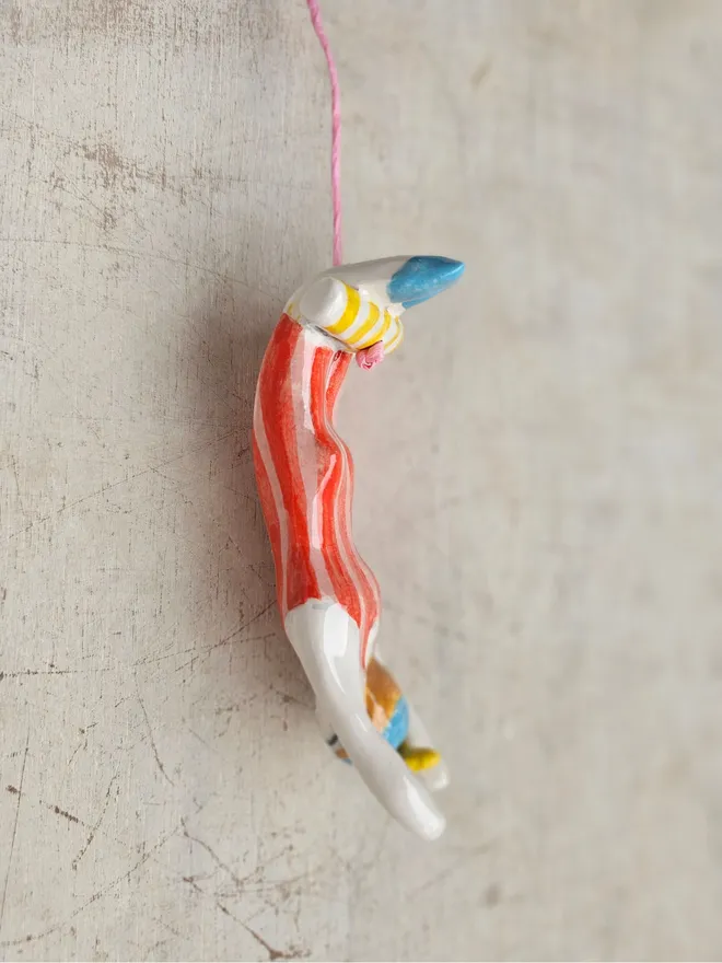 female acrobat hanging upside down in a red and pink stripe suit, side view