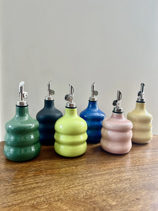 a collection of 6 colourful chubby oil bottles with wavy sides on a wooden table. 
