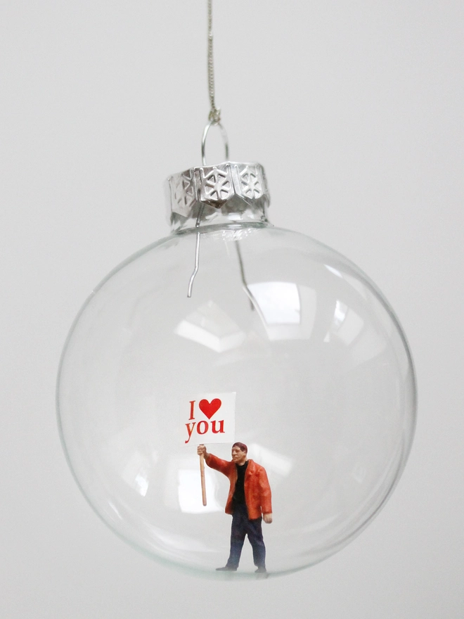 miniature man figure holding a sign that says I LOVE YOU in a glass christmas bauble
