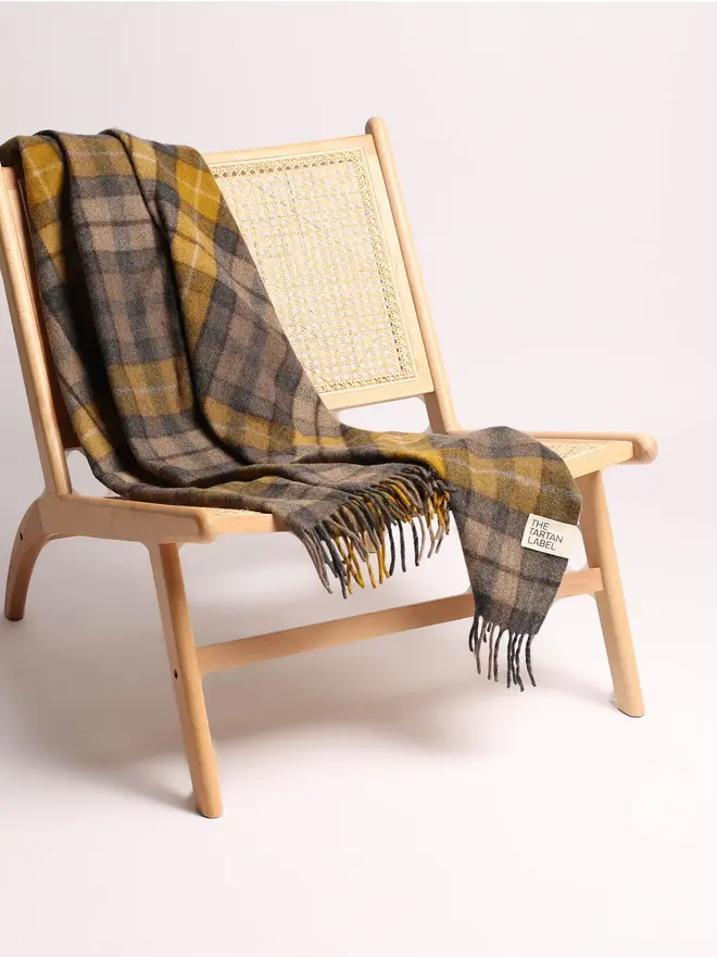 Buchanan Natural Recycled Wool Blanket, a yellow and brown blanket draped over a wooden chair on a white surface against a plain backdrop. 