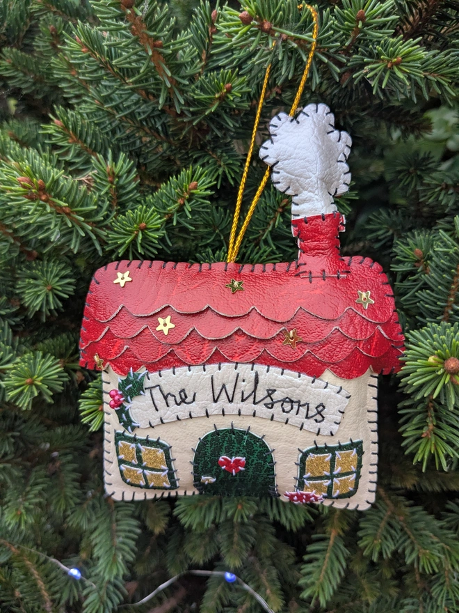 Hand stitched personalised Christmas house decoration made from vegan-friendly faux leather, featuring a red roof, gold stars and a family name banner.