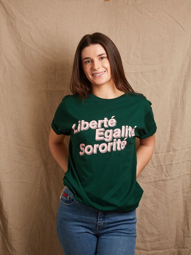Model is wearing a forest green cotton t-shirt with the slogan Liberté, Egalité, Sororité in pale pink written on the front
