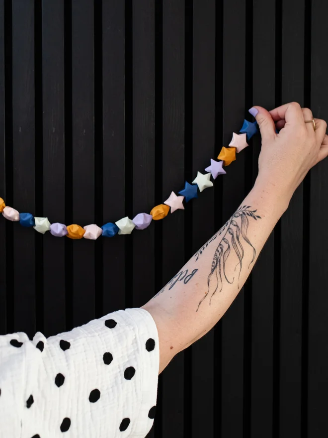 Woman extending an arm to hang a star garland on the wall.