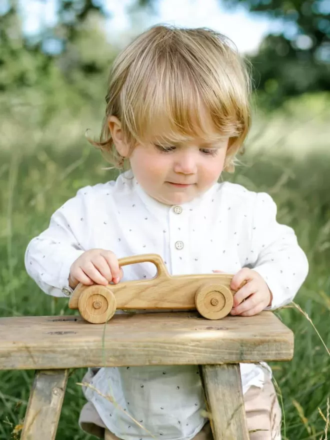 little baby playing with the wooden toy car outside