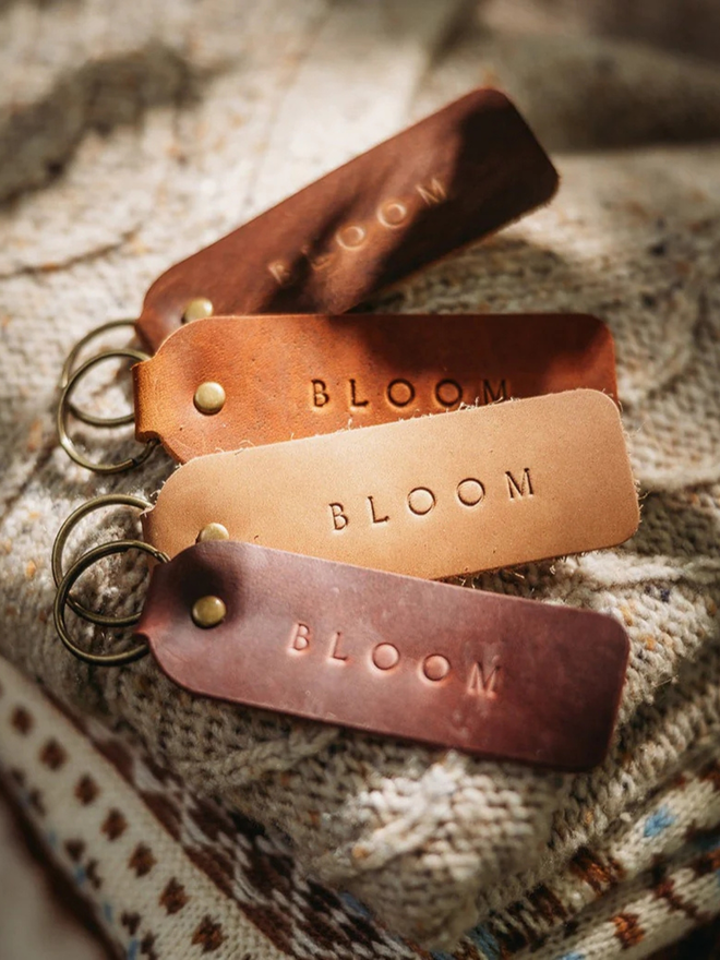 encouraging leather keyring. brown keyrings laid atop a blanket, embossed with the word 'bloom'.
