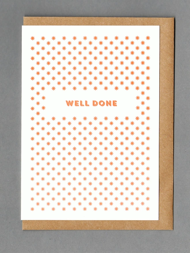 White card with orange stars and orange text reading 'WELL DONE' with a kraft envelope behind it