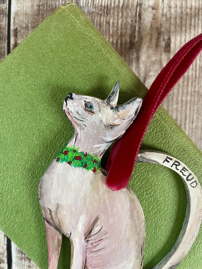Hairless Sphynx Cat Christmas Decoration strung with red velvet ribbon and placed on a green book