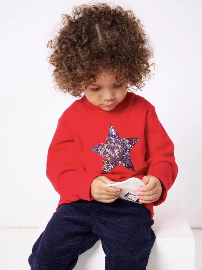 A little boy wearing a red tee with a Liberty star print star sewn on the front
