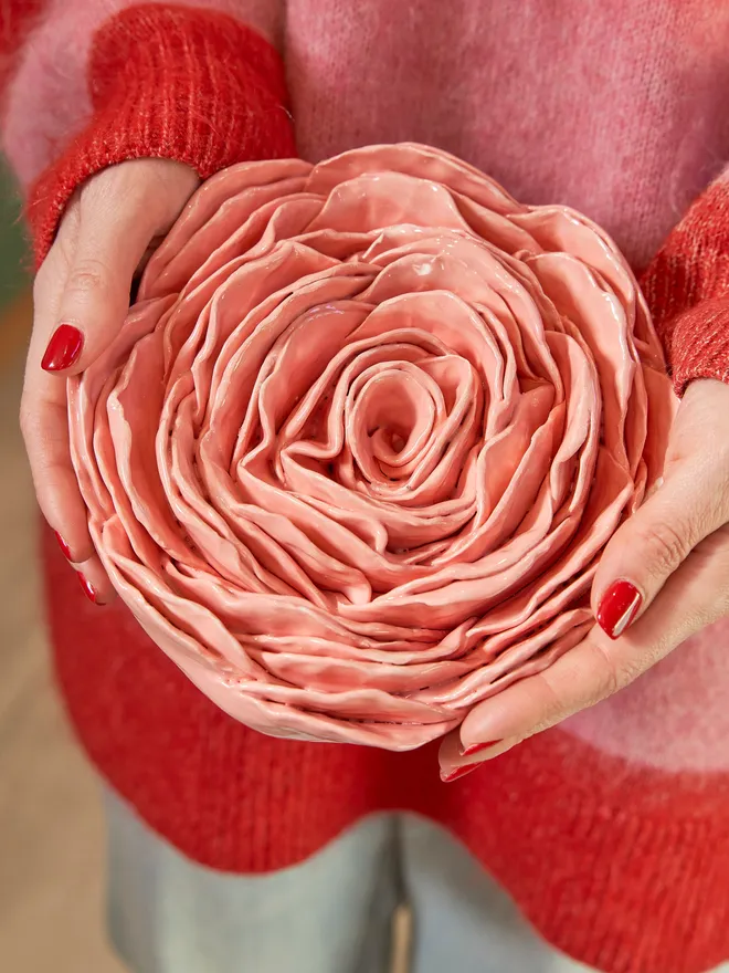 Large sized ceramic rose held up by a woman in a pink and red striped jumper