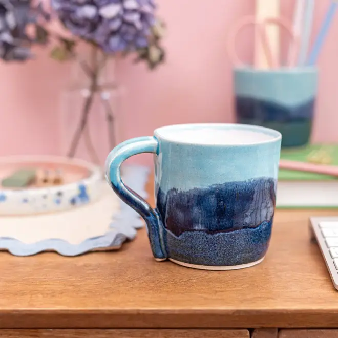 Landscape Standard Mug, a colourful mug placed on a desk. It is accompanied by flowers. 
