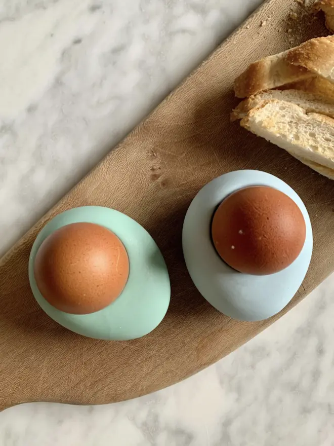 2 colourful egg cups with brown eggs on wood board