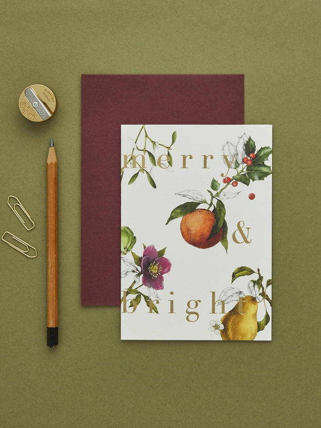 ivory based christmas card with festive hand drawn botanicals with gold foil wording and a burgundy envelope