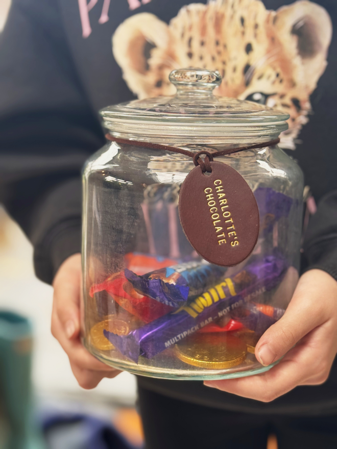 a glass jar with chocolate in, a leather label with 'charlotte's chocolates' stamped on the brown tag with gold writing.