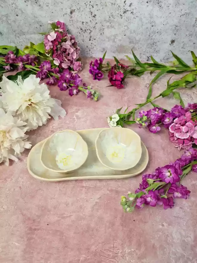 Serveware, Small serving dish crafted from stoneware clay and glazed in Dream Catcher glaze with creams, whites, hints of pink, lilac and specks of metallic gold. Two bowls and an oval dish, tapas dish, snack dish, gift, handmade, homeware, pink background, flowers