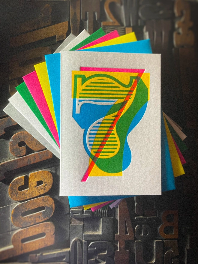 Handmade letterpress 7th birthday card featuring bold overlapping numerals printed in vibrant fluorescent cyan, magenta and yellow inks. Each card is individually hand printed using traditional letterpress techniques on luxury paper stock, creating a beautifully tactile finish with a deep impression and rich layered colours inspired by the CMYK printing process. Printed on a traditional letterpress from 1915. A wonderful artisan printed birthday card.