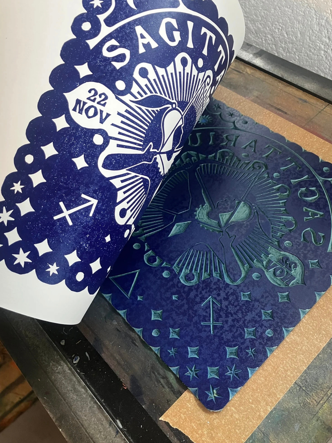 saggitarius zodiac linocut. a linocut archer and zodiac symbols printed on a blue background.