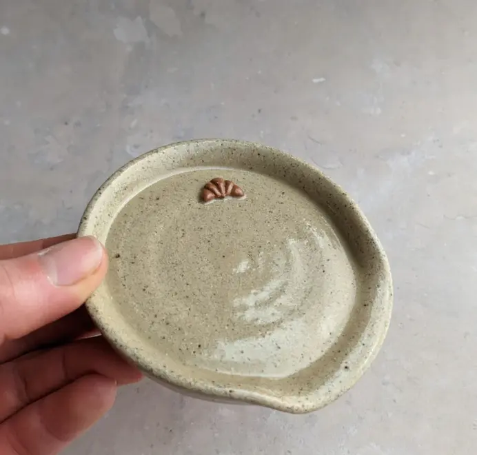 Croissant stoneware spoon rest in biscuit glaze against a grey marble background.