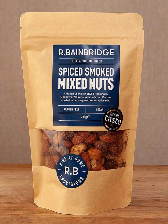 Spiced Smoked Nuts Packet, a pack of nuts sitting on a wooden surface against a plain backdrop. 