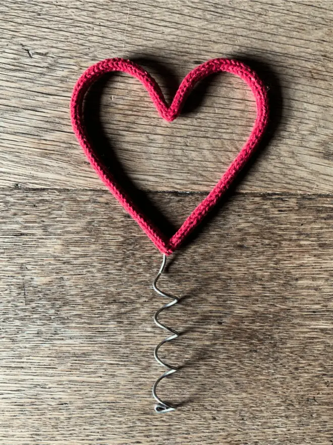 A red string wrapped wire heart shaped Christmas tree topper on an oak table