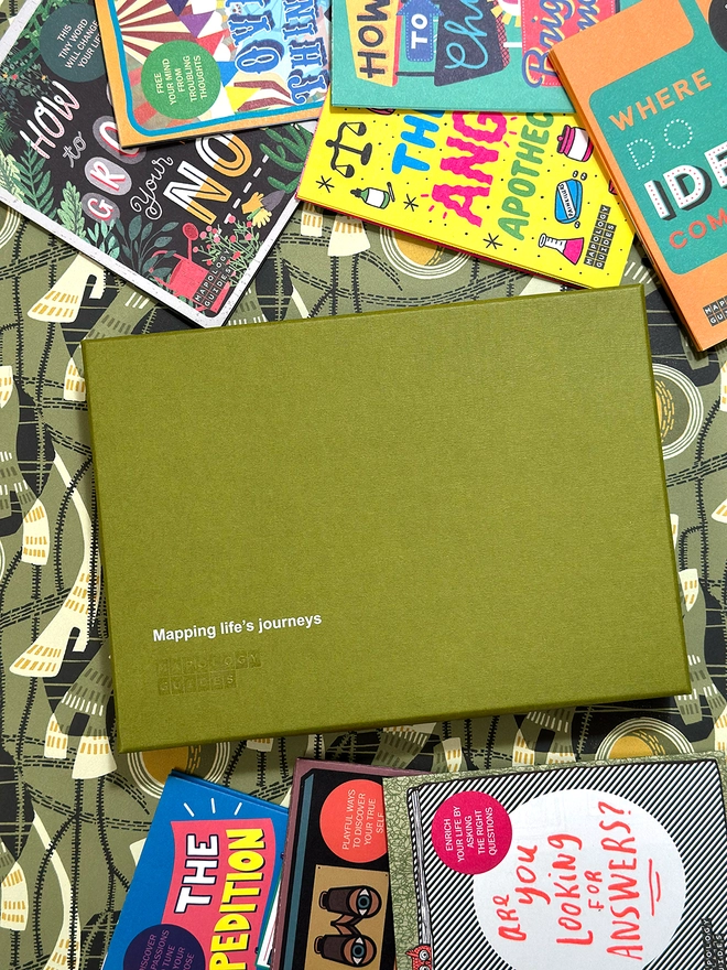 An olive green box with printed logo surrounded by multi-coloured front covers of maps