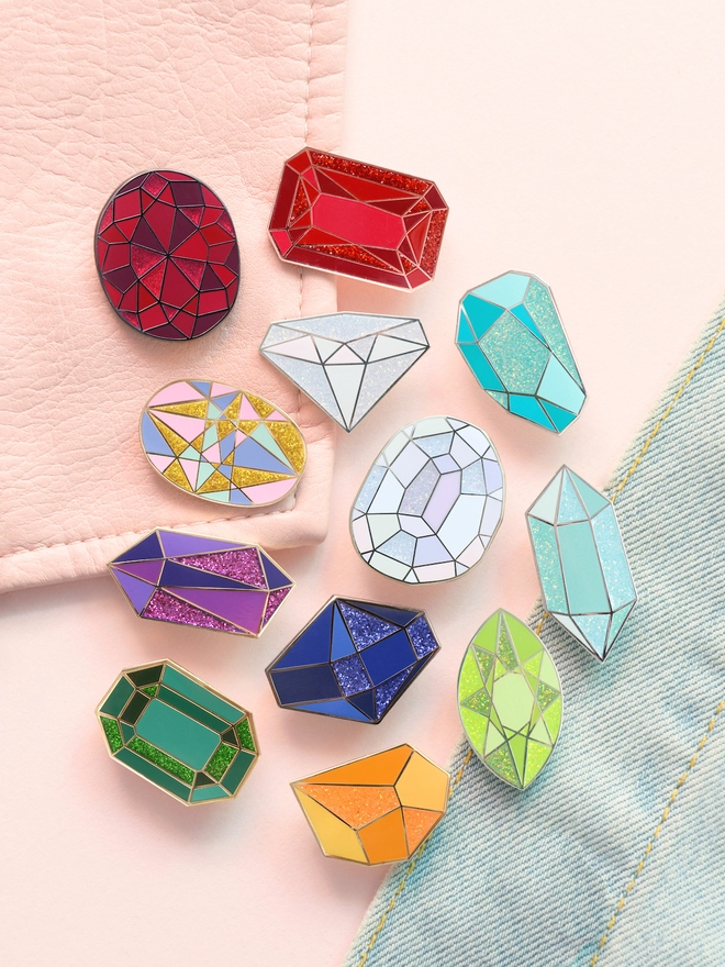 group of sparkly birthstone enamel pins laying on a pink jacket