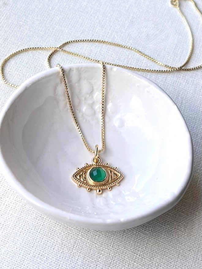 gold evil eye charm necklace with green stone in the centre on a gold box chain 