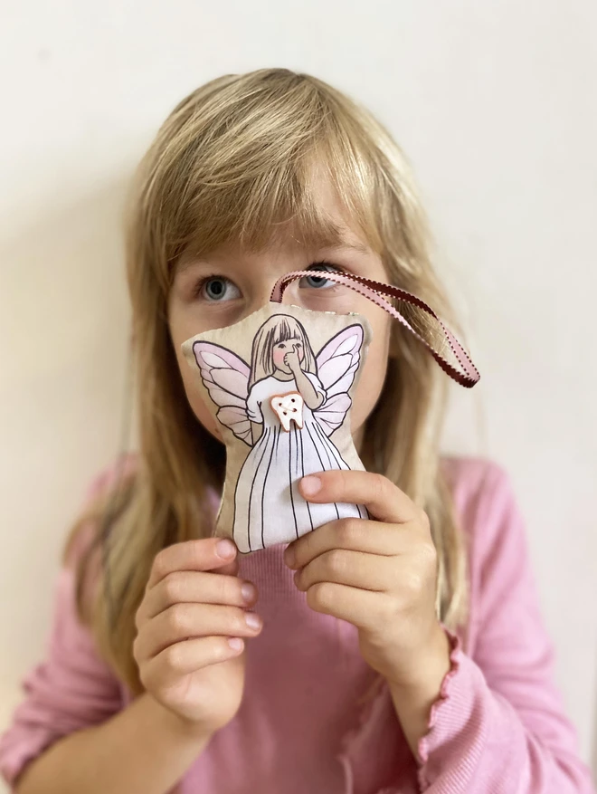 little girl with blonde hair holding a small tooth fairy decoration