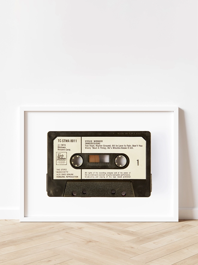 stevie wonder innervisions cassette tape print. framed print propped up against white wall on wooden floor.
